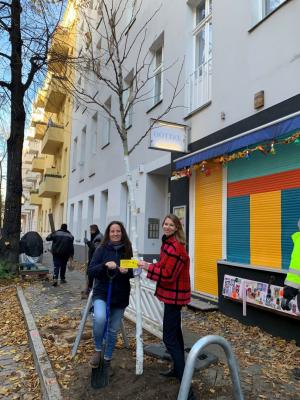 Zwei Personen pflanzen einen Baum vor einem Wohnhaus