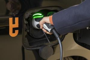 Eine Person steckt ein Ladekabel in ein mit dem BEA-Logo versehenes E-Auto.