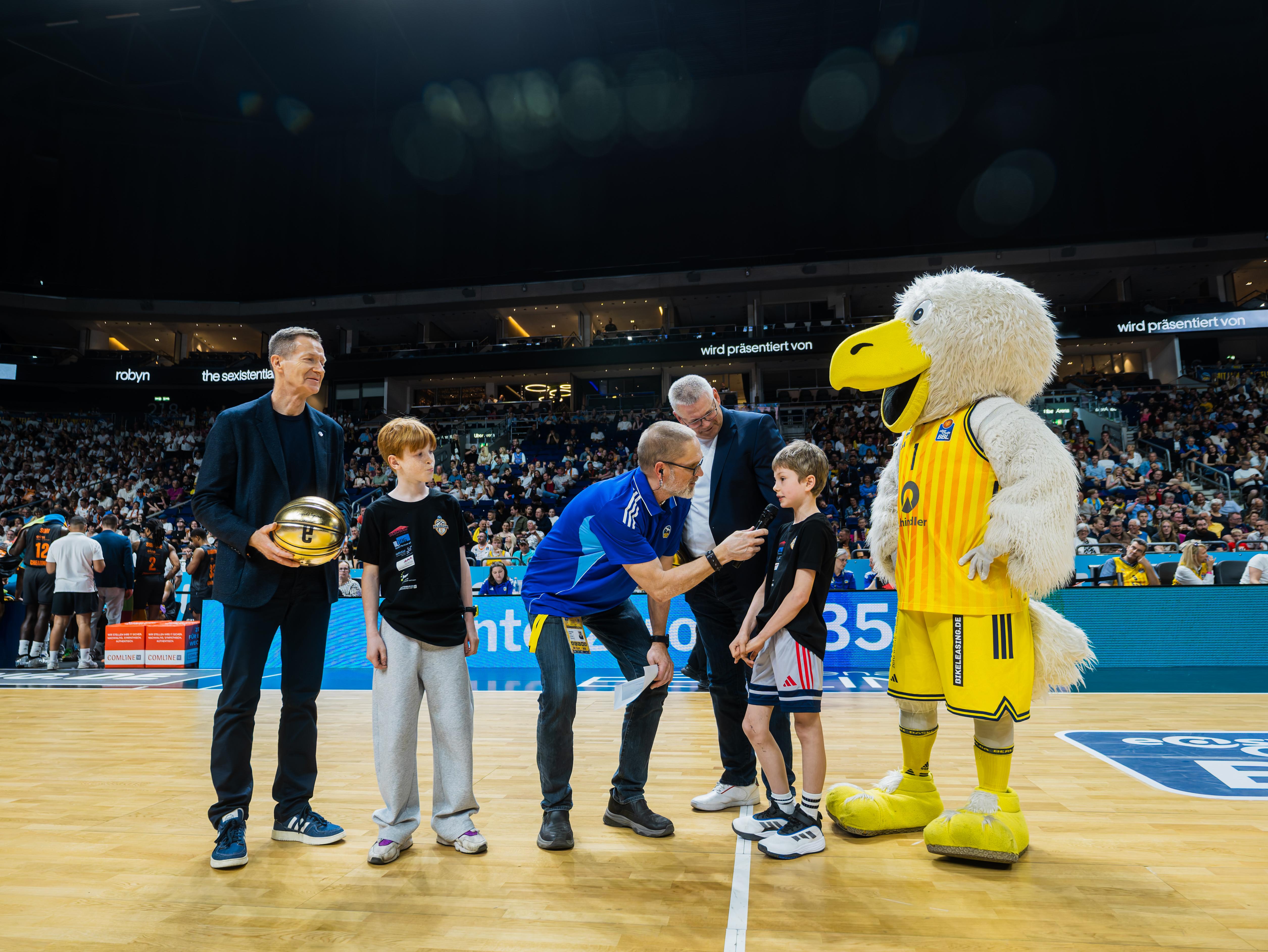 BEA-Geschäftsführer Michael Geißler, die Kiezcamp-Gewinner Leo und Fritz, Hallensprecher Tom Böttcher, "Charlotte"-Vorstand Dirk Enzesberger und der Albatros auf dem Spielfeld von ALBA Berlin. Foto: Tilo Wiedensohler
